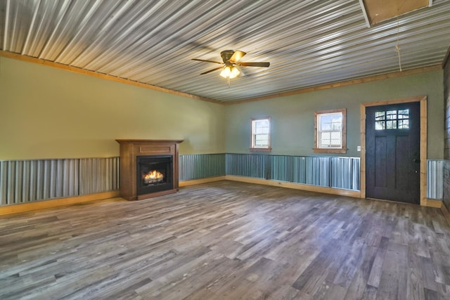 unfurnished living room with a warm lit fireplace, wood finished floors, and a ceiling fan