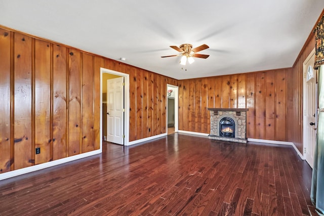 unfurnished living room featuring baseboards, a stone fireplace, dark wood-style floors, and a ceiling fan