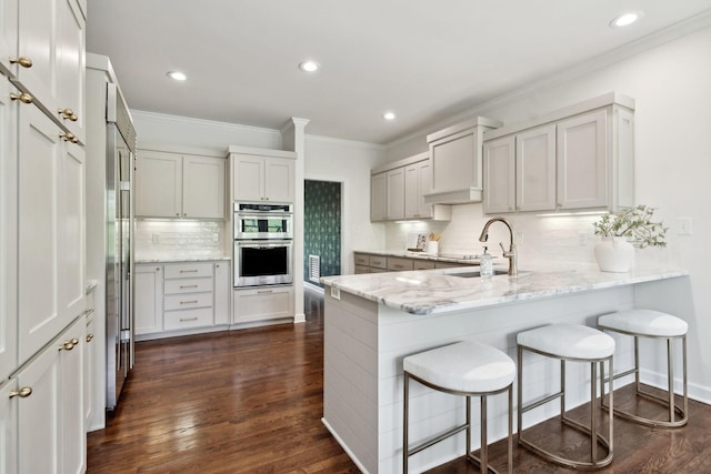kitchen featuring double oven, light stone counters, crown molding, decorative backsplash, and a peninsula