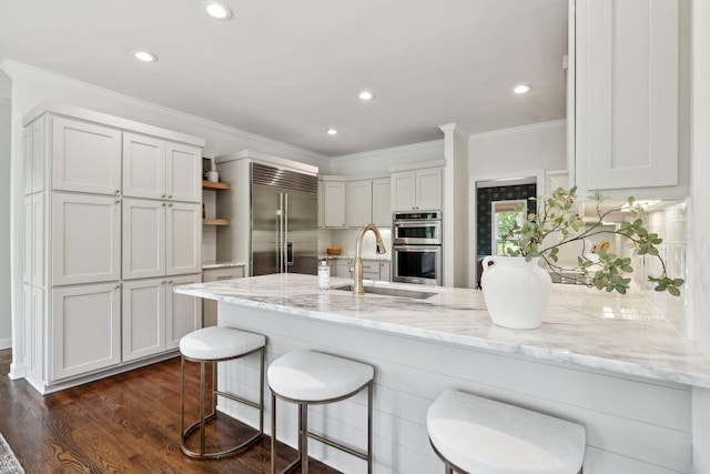 kitchen featuring stainless steel appliances, a peninsula, a sink, open shelves, and light stone countertops