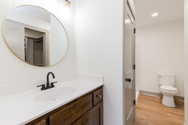 bathroom with baseboards, toilet, recessed lighting, wood finished floors, and vanity
