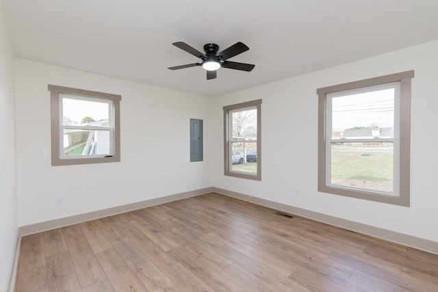spare room featuring light wood-type flooring, visible vents, electric panel, baseboards, and ceiling fan