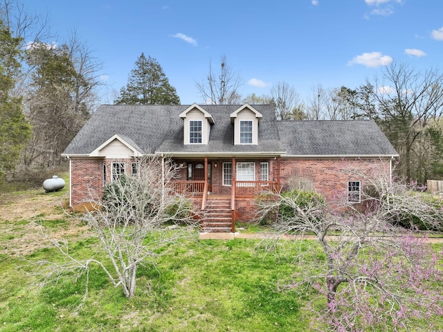 cape cod-style house featuring a porch, brick siding, and a shingled roof