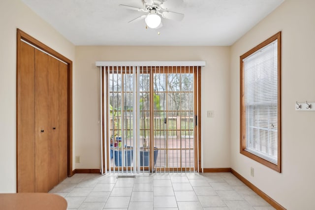 interior space with light tile patterned floors, a ceiling fan, and baseboards