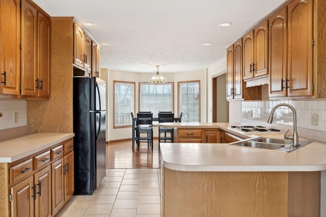 kitchen with a sink, a peninsula, light countertops, and freestanding refrigerator