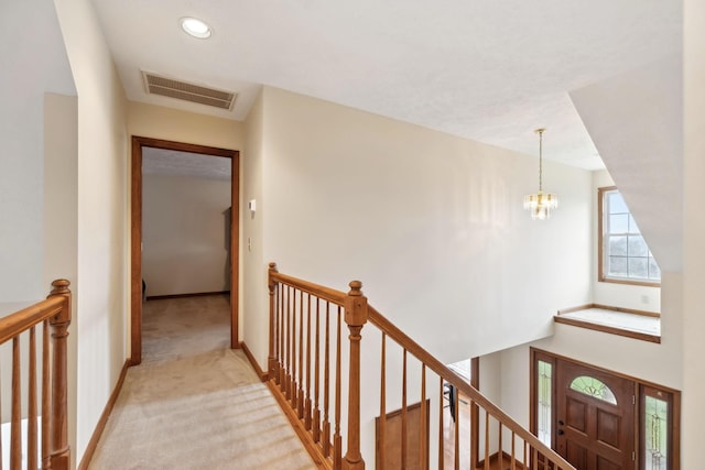 corridor featuring visible vents, baseboards, an upstairs landing, light colored carpet, and a chandelier