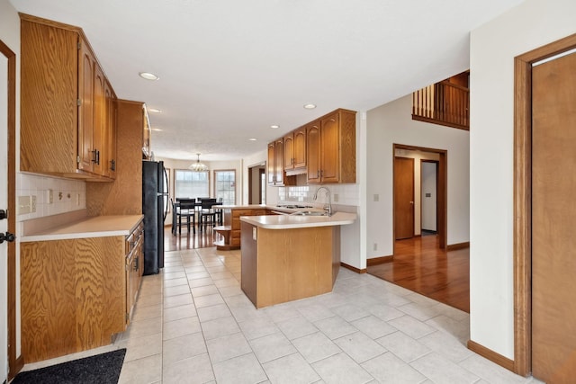 kitchen featuring light tile patterned floors, a peninsula, freestanding refrigerator, decorative backsplash, and light countertops