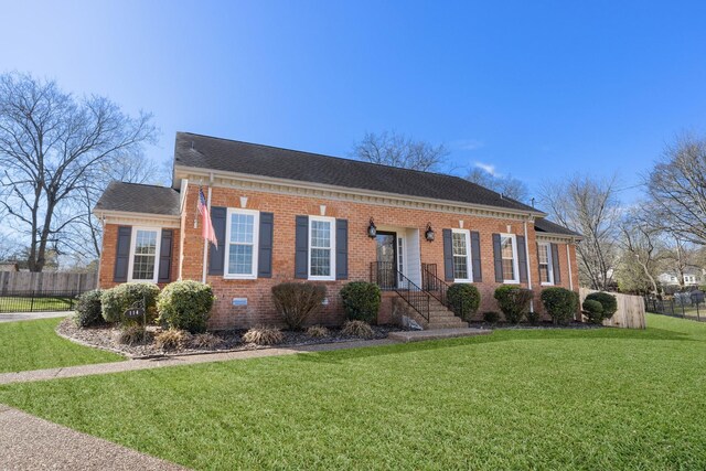 view of front facade with brick siding, a shingled roof, a front yard, and fence