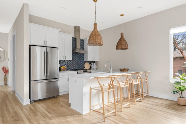kitchen featuring wall chimney exhaust hood, a sink, high quality fridge, light wood-style flooring, and a breakfast bar area