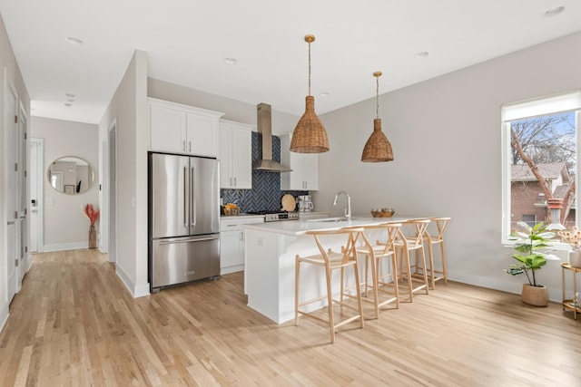 kitchen with tasteful backsplash, high end fridge, light wood-style flooring, wall chimney exhaust hood, and a kitchen bar