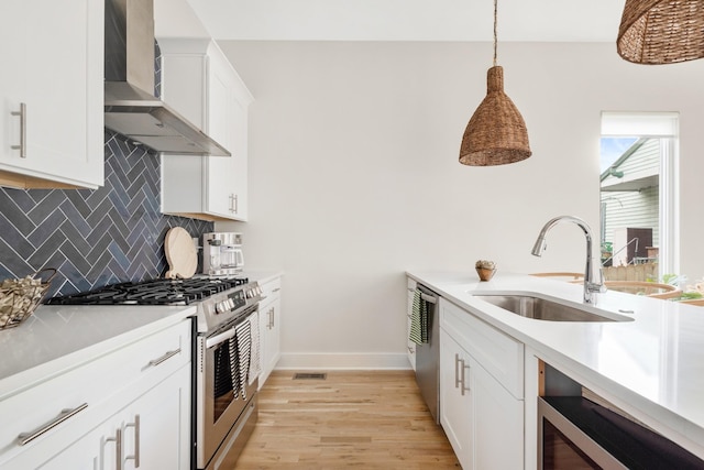 kitchen featuring a sink, wall chimney range hood, light wood finished floors, stainless steel appliances, and decorative backsplash