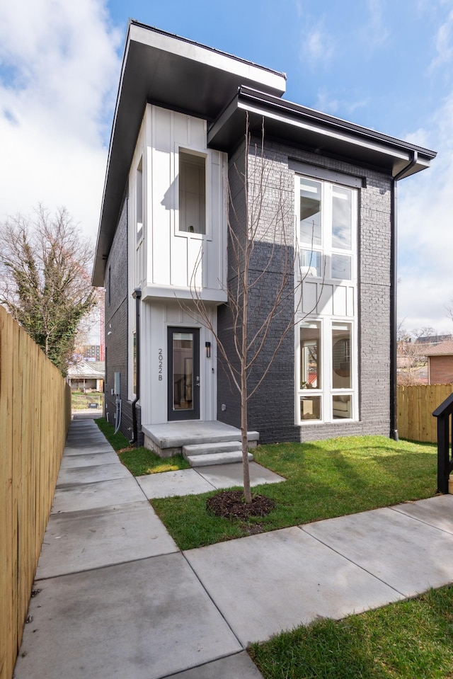 contemporary home with brick siding, a front yard, and fence