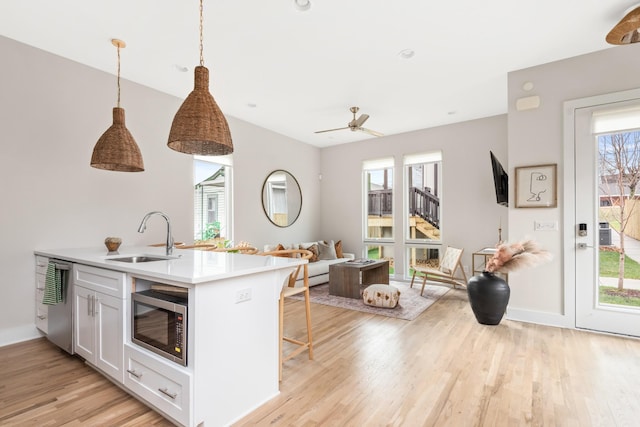 kitchen featuring open floor plan, white cabinetry, appliances with stainless steel finishes, light wood finished floors, and a sink