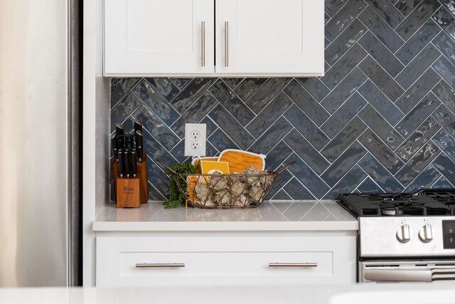 interior space featuring gas range, light countertops, backsplash, and white cabinets