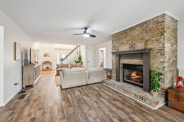 living area with visible vents, stairs, a fireplace, ceiling fan, and dark wood-type flooring