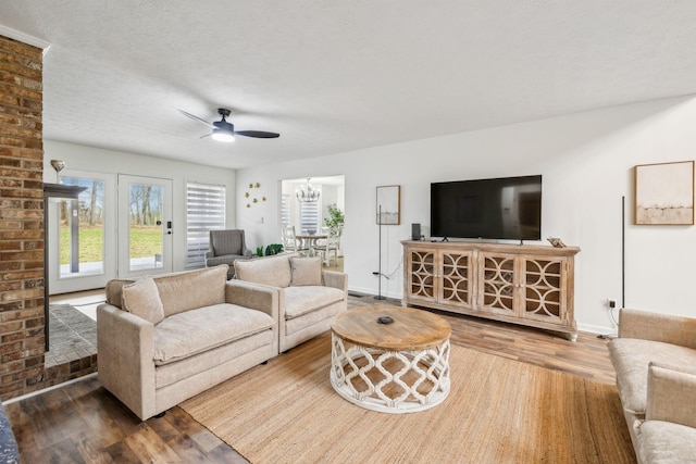 living area featuring ceiling fan with notable chandelier, baseboards, a textured ceiling, and wood finished floors