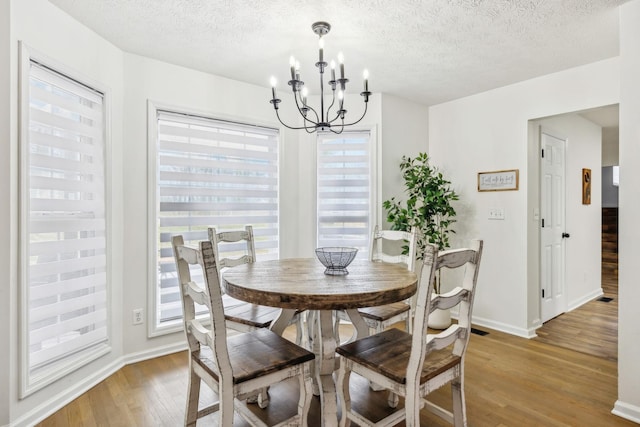 dining space with light wood-style flooring, baseboards, a chandelier, and a textured ceiling