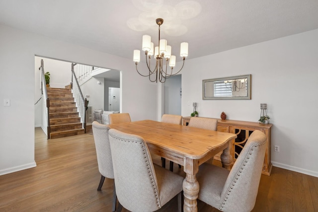 dining space featuring a notable chandelier, baseboards, stairs, and wood finished floors