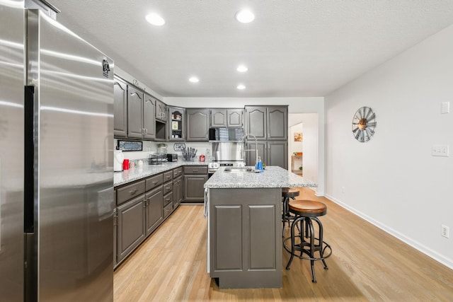 kitchen featuring gray cabinets, a breakfast bar area, light wood-type flooring, and freestanding refrigerator