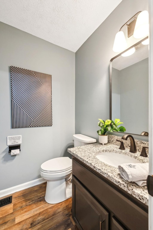 bathroom with vanity, toilet, a textured ceiling, visible vents, and wood finished floors