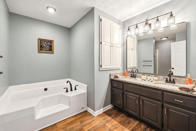 full bath featuring wood finished floors, a textured ceiling, a sink, double vanity, and a bath