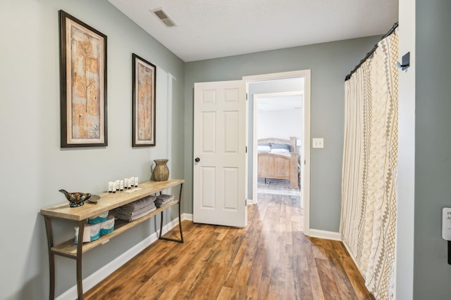 corridor featuring baseboards, visible vents, wood finished floors, and a textured ceiling