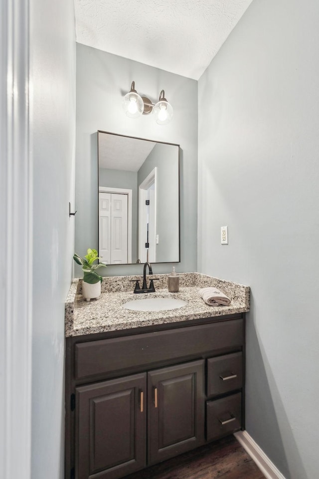 bathroom featuring vanity, a textured ceiling, baseboards, and wood finished floors