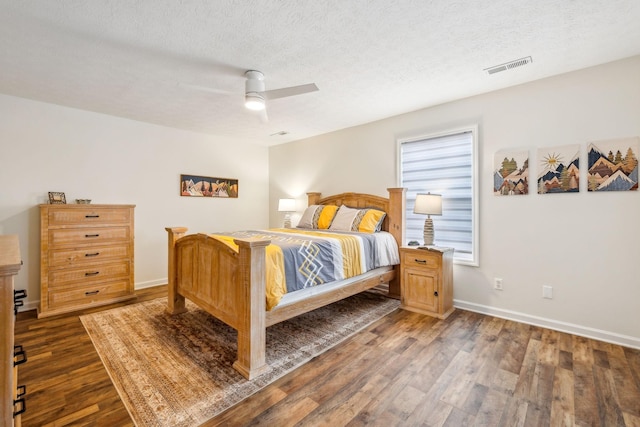bedroom with baseboards, a textured ceiling, visible vents, and wood finished floors