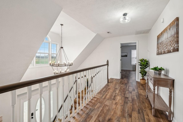 hall with an upstairs landing, a chandelier, a textured ceiling, visible vents, and wood finished floors