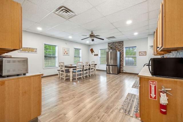 kitchen with light wood-type flooring, a wealth of natural light, freestanding refrigerator, black microwave, and ceiling fan