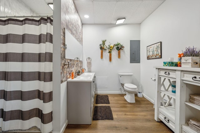 bathroom featuring electric panel, toilet, vanity, wood finished floors, and a paneled ceiling