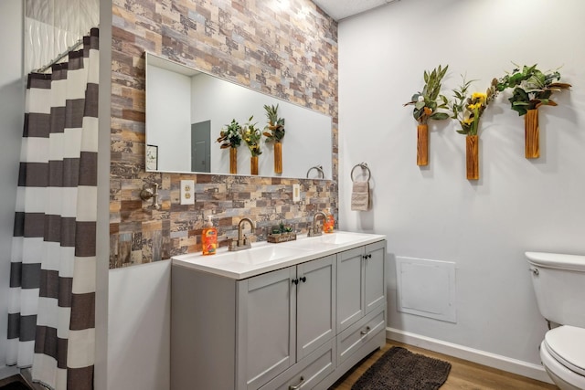 bathroom with toilet, a sink, double vanity, and baseboards