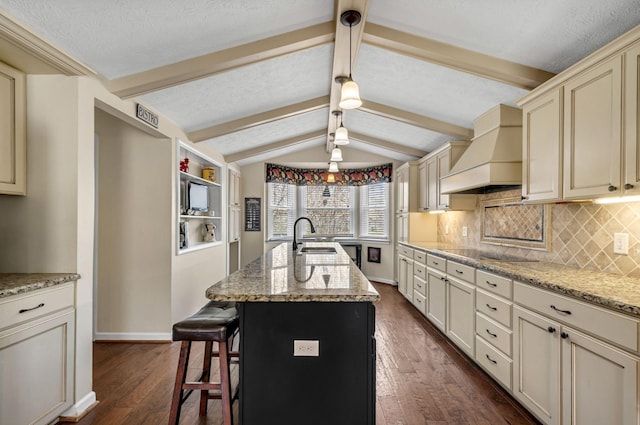 kitchen featuring vaulted ceiling with beams, a sink, custom range hood, cream cabinetry, and black electric cooktop