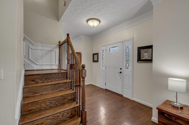 foyer with ornamental molding, a textured ceiling, hardwood / wood-style floors, baseboards, and stairs