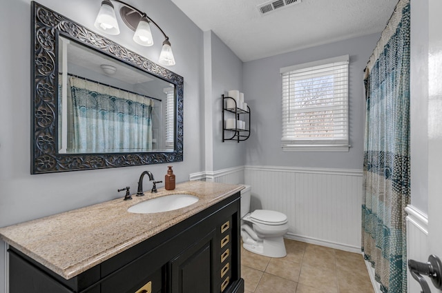 full bath featuring visible vents, toilet, a textured ceiling, wainscoting, and tile patterned flooring
