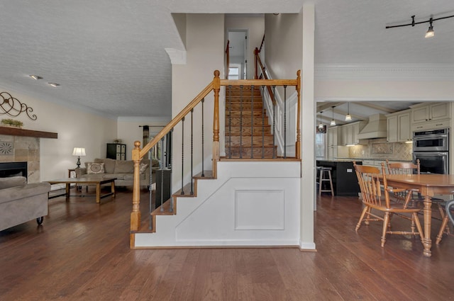 stairway featuring wood finished floors, a tile fireplace, ornamental molding, track lighting, and a textured ceiling