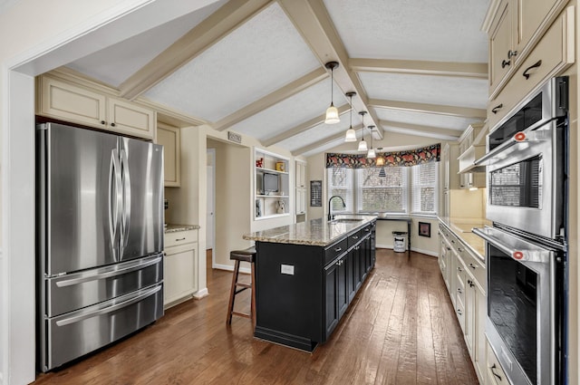 kitchen with dark wood-type flooring, cream cabinetry, a sink, stainless steel appliances, and vaulted ceiling with beams