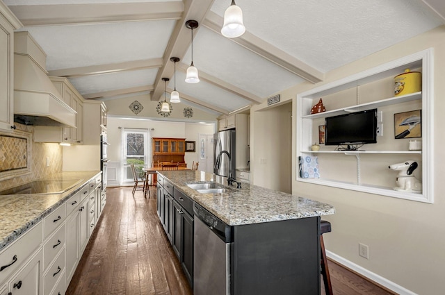 kitchen featuring a kitchen island with sink, a sink, lofted ceiling with beams, appliances with stainless steel finishes, and dark wood-style flooring