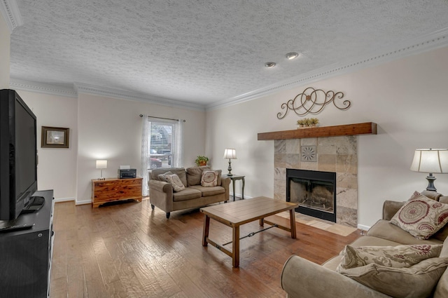 living area with a textured ceiling, a tile fireplace, wood-type flooring, and ornamental molding