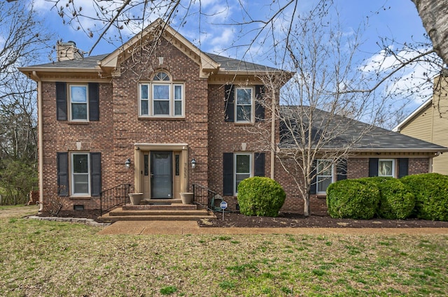 view of front of house featuring brick siding, a chimney, and a front yard
