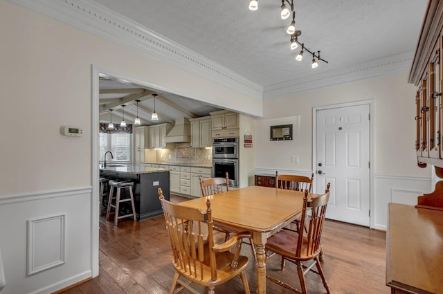 dining room with crown molding, dark wood finished floors, a wainscoted wall, lofted ceiling with beams, and a textured ceiling