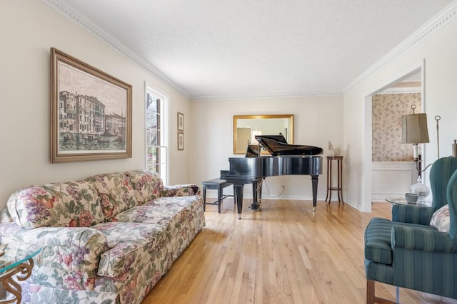 living area featuring a wainscoted wall, a textured ceiling, light wood-style flooring, and crown molding