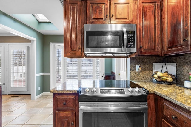 kitchen featuring light tile patterned floors, baseboards, a peninsula, appliances with stainless steel finishes, and backsplash