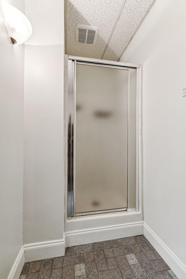 full bath featuring a shower stall, stone finish floor, baseboards, and visible vents