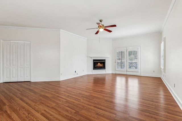 unfurnished living room featuring ornamental molding, a ceiling fan, a warm lit fireplace, wood finished floors, and baseboards