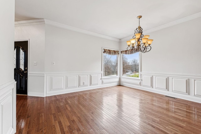 spare room with a notable chandelier, visible vents, ornamental molding, and hardwood / wood-style flooring