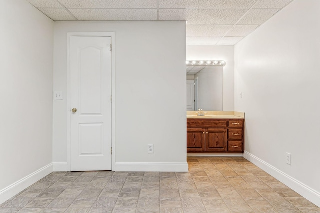 unfurnished bedroom with ensuite bath, baseboards, a drop ceiling, and a sink