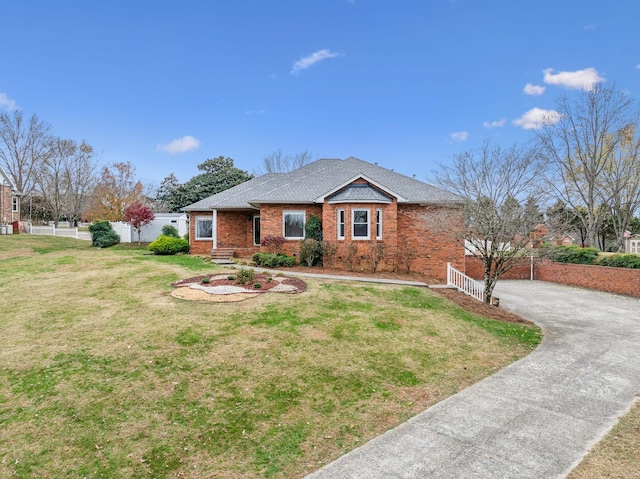 ranch-style home featuring brick siding, a front lawn, fence, roof with shingles, and driveway