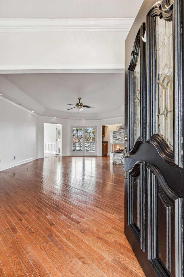 unfurnished living room with crown molding, ceiling fan, baseboards, a stone fireplace, and light wood-style floors