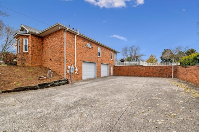 view of side of property with brick siding, fence, a garage, and driveway